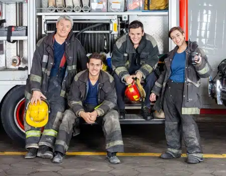 A group of firefighters in uniform posing together in front of a fire truck, showcasing teamwork and camaraderie.