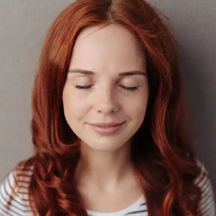 Close-up of a red-haired woman with her eyes closed, exuding calmness and peace.