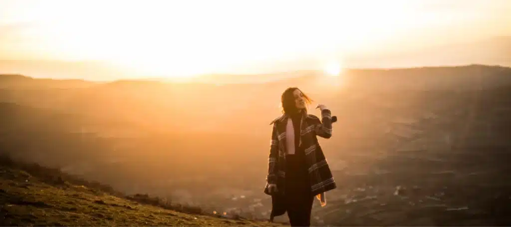 Silhouetted woman walking on a hilltop at sunrise, surrounded by breathtaking golden light and scenic views.