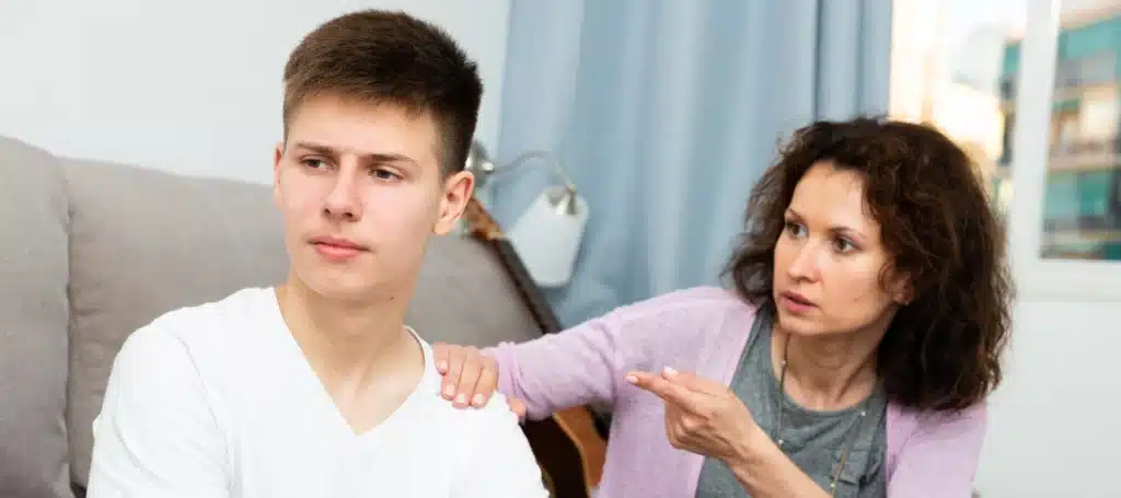 A frustrated mother arguing with her teenage son. The son looks away while the mother gestures at him.