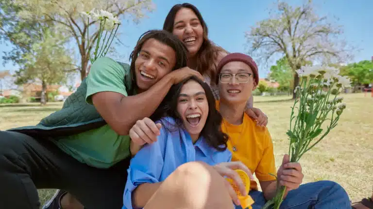 A group of diverse young friends laughing in a park. They are enjoying the outdoors and holding flowers.
