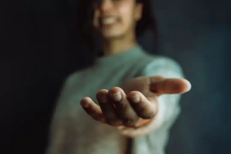 A close-up of an outstretched hand offering a welcoming gesture, set against a softly blurred background.