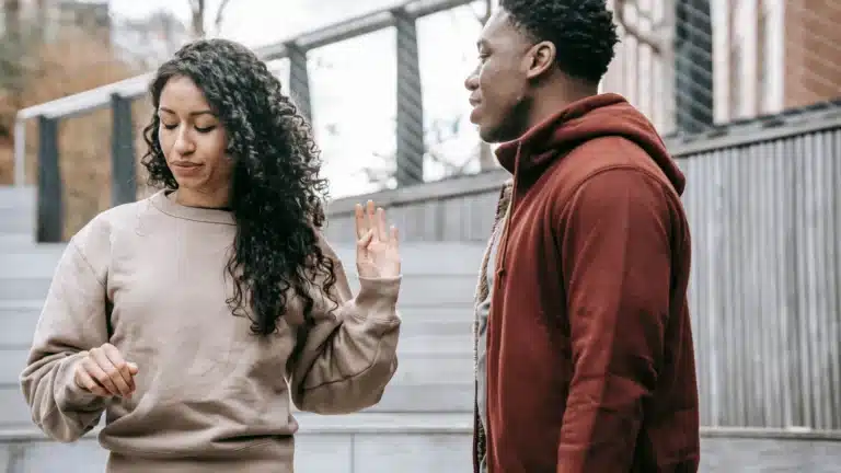 A woman rejecting a conversation with a man outdoors. She raises her hand while looking away as he tries to engage.