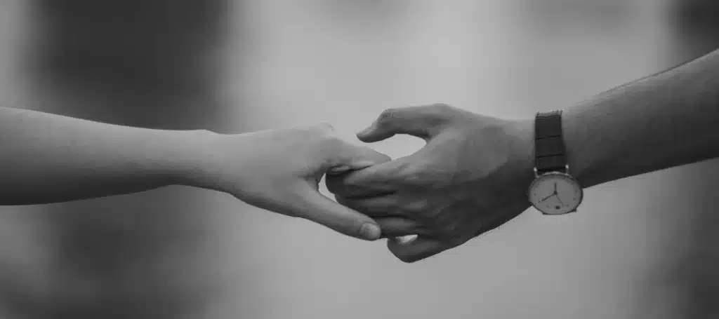 A close-up black and white image of two hands gently holding each other.