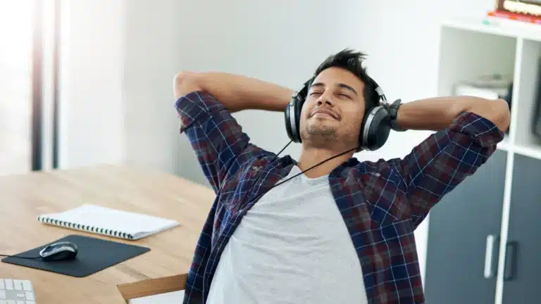 Man wearing headphones, leaning back in a chair with his hands behind his head, relaxing in a home office setting.