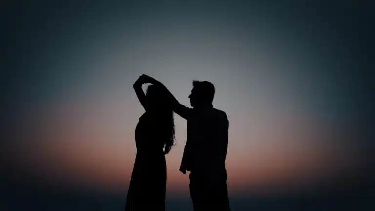 A silhouetted man and woman dancing together against a colorful sunset sky.