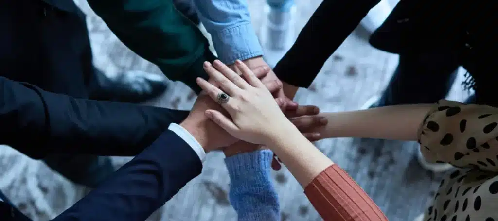 A group of people placing their hands together in a stack, symbolizing teamwork and cooperation.